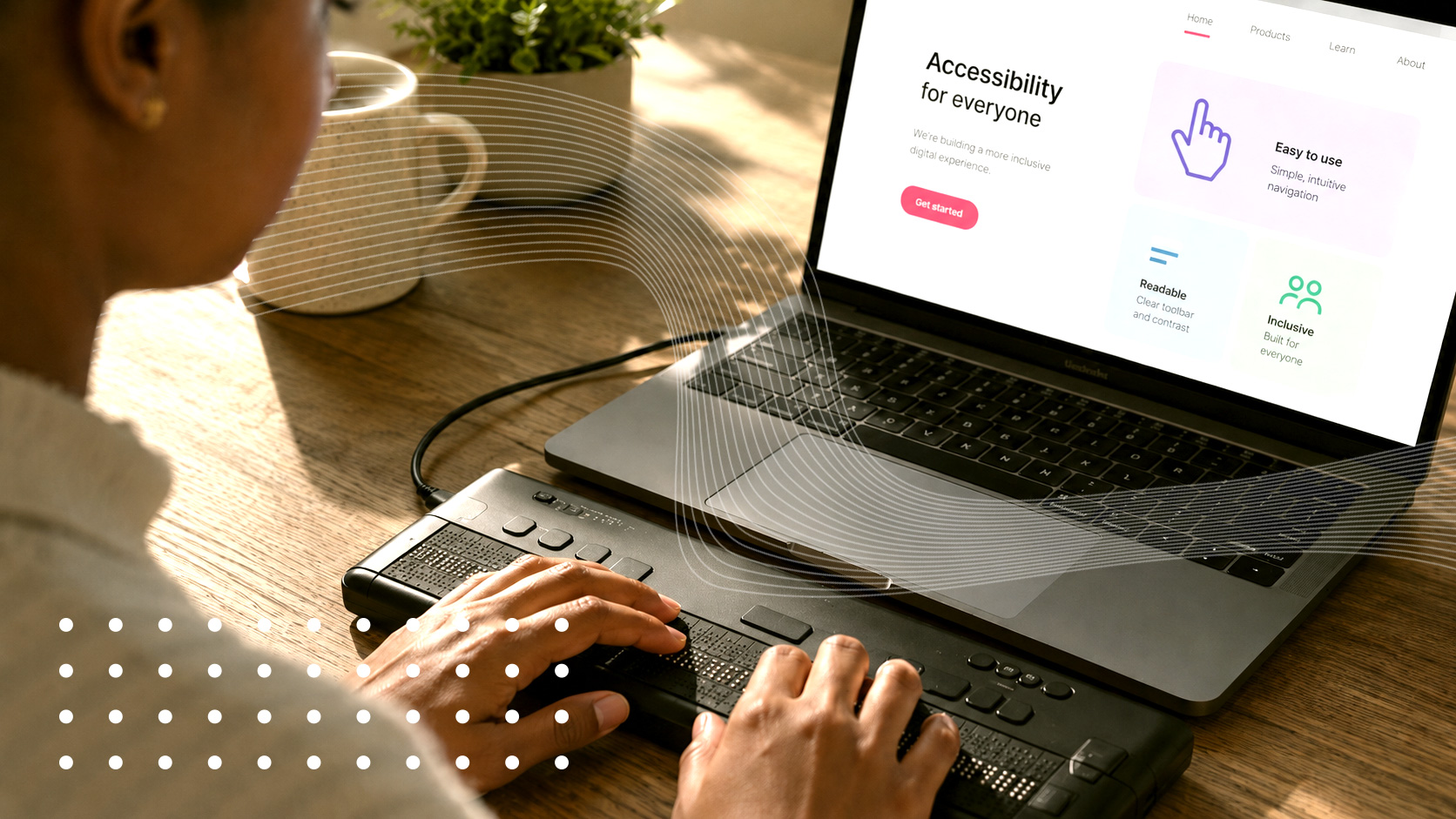 A person uses a braille display while viewing an accessibility-focused website on a laptop