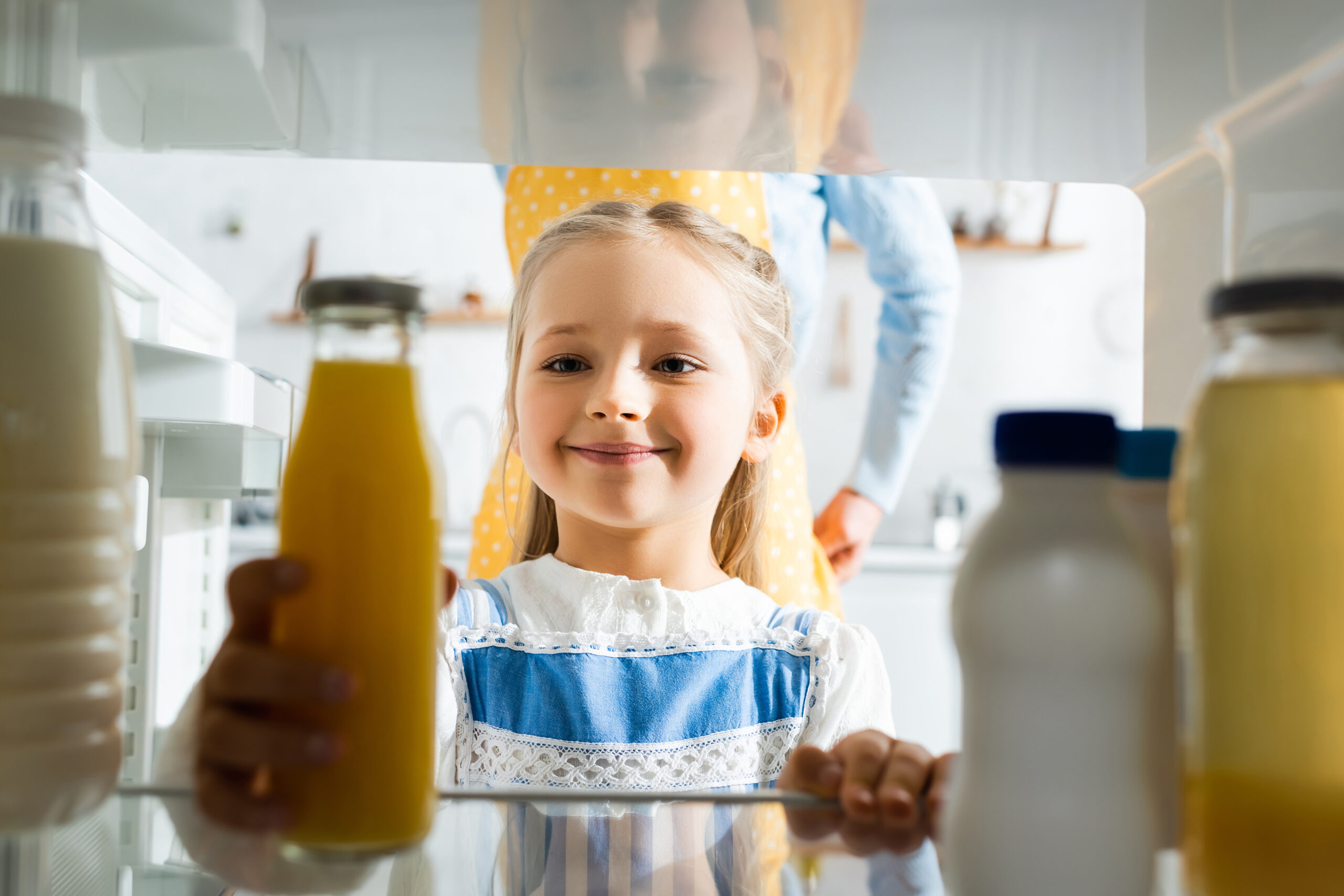selective focus of smiling kid taking orange juice from fridge