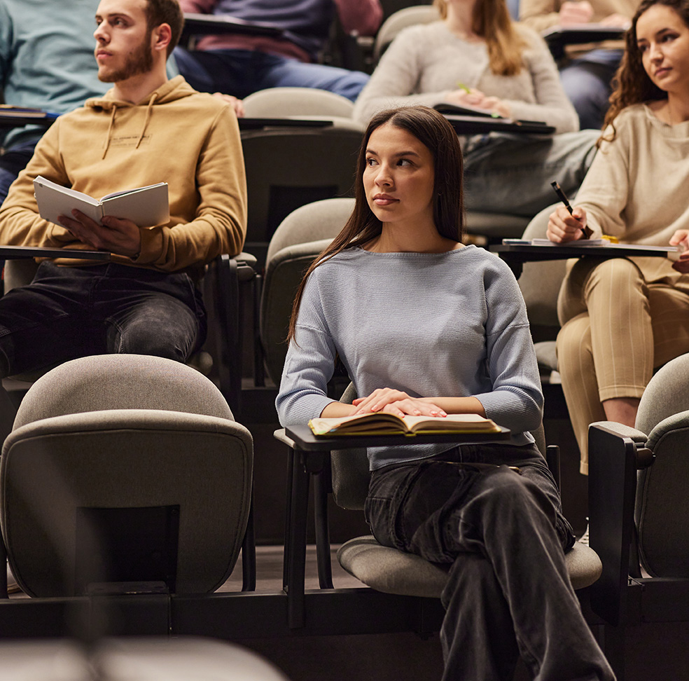 Large group of university students paying attention on a lecture at amphitheater. Focus is on woman in the foreground.